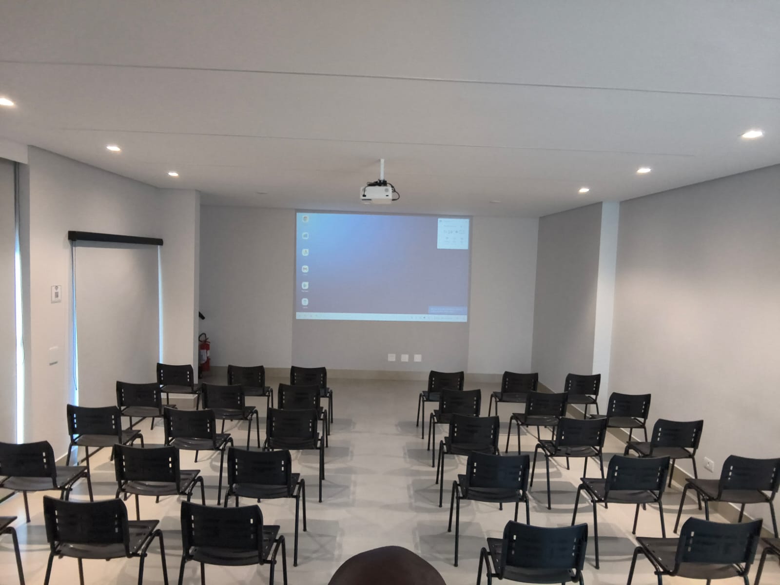 Auditório montado com cadeiras pretas e tela de projeção