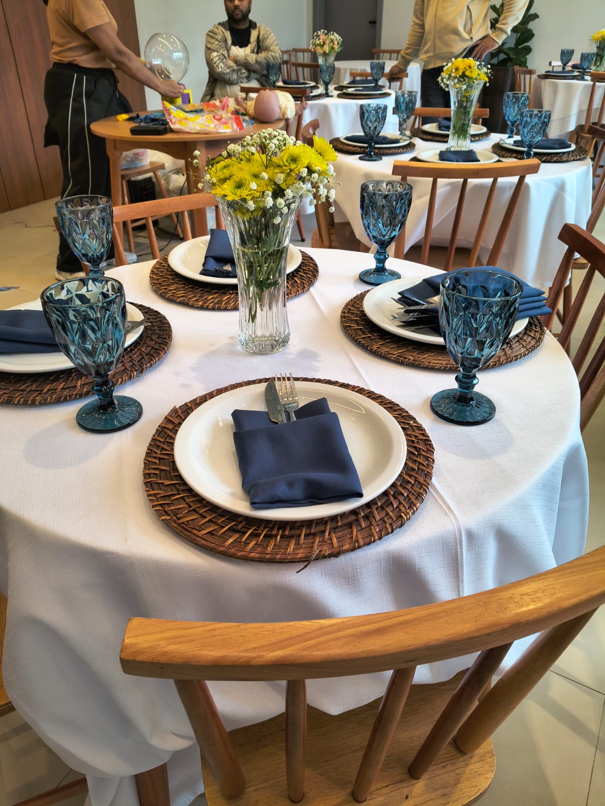 Mesa decorada com taças azuis, flores amarelas e louça branca