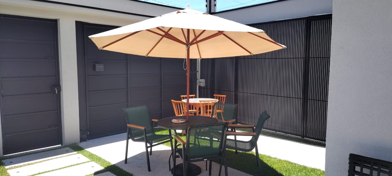 Área externa com mesa, cadeiras e ombrelone ao sol