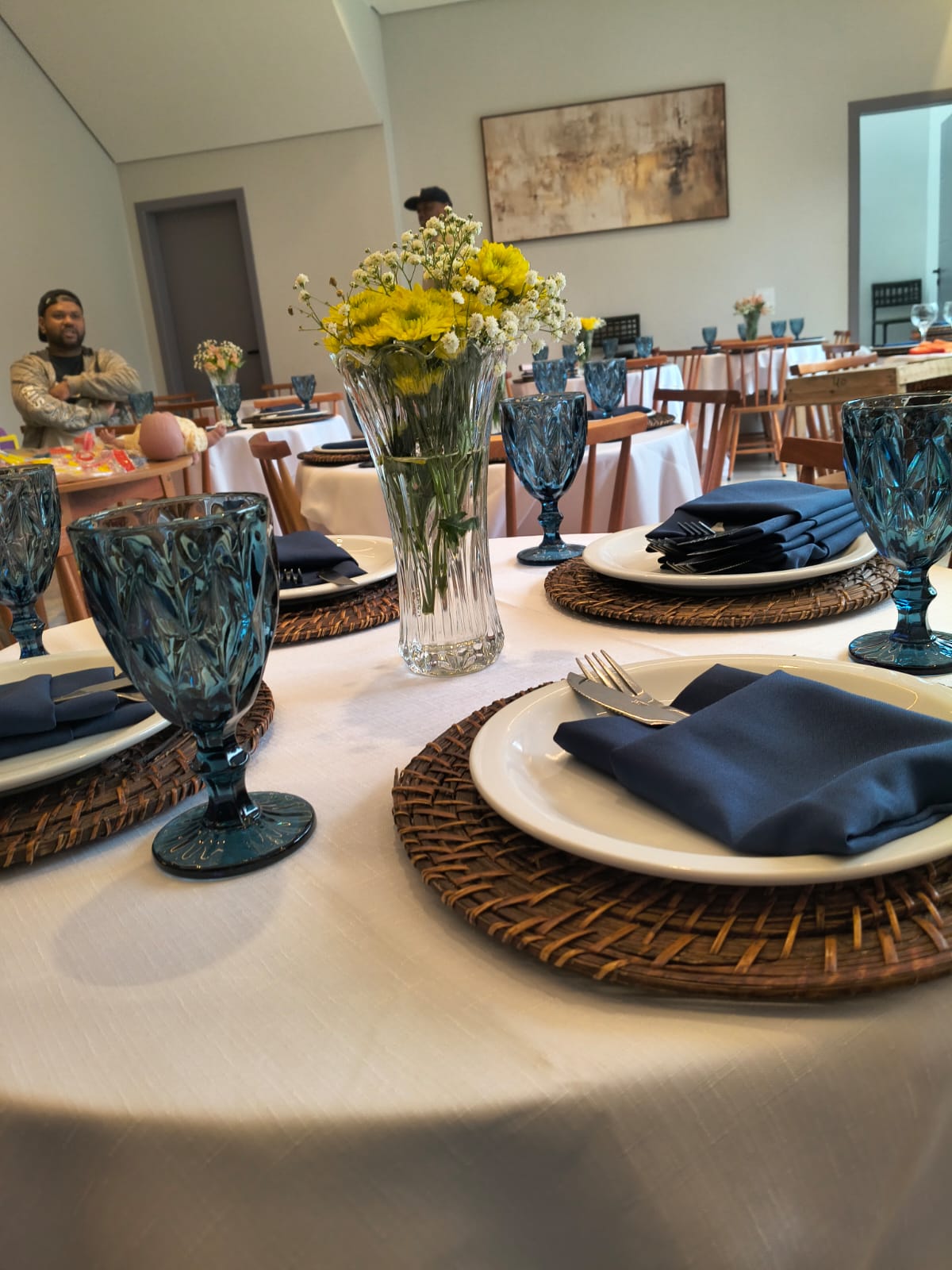 Mesa posta com louça branca, taças azuis e flores no salão de festas em Guarulhos