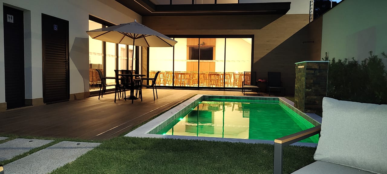 Piscina e deck à noite com vista para as portas de vidro do salão